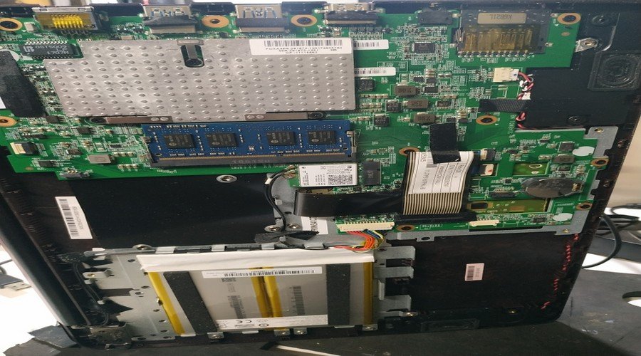 Notebook aberto na bancada durante manutenção, com placa-mãe, memória e bateria à vista